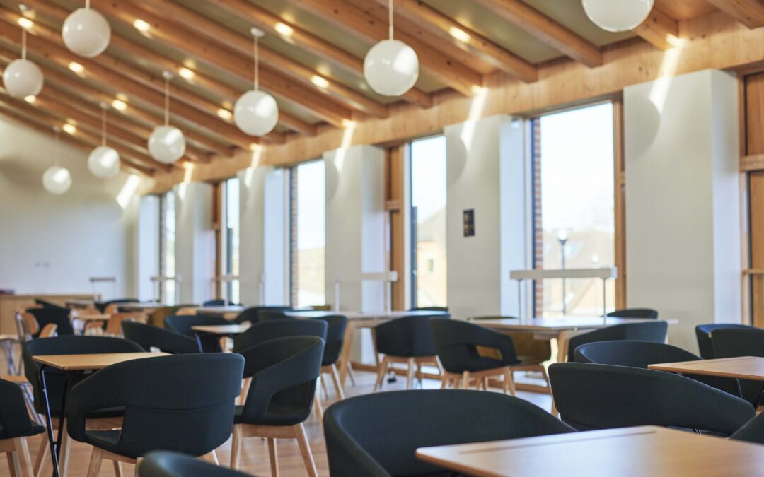 Bright classroom at Worth School with wooden ceiling beams, round pendant lights, and tables and chairs, used for Metis Institute psychotherapy training.
