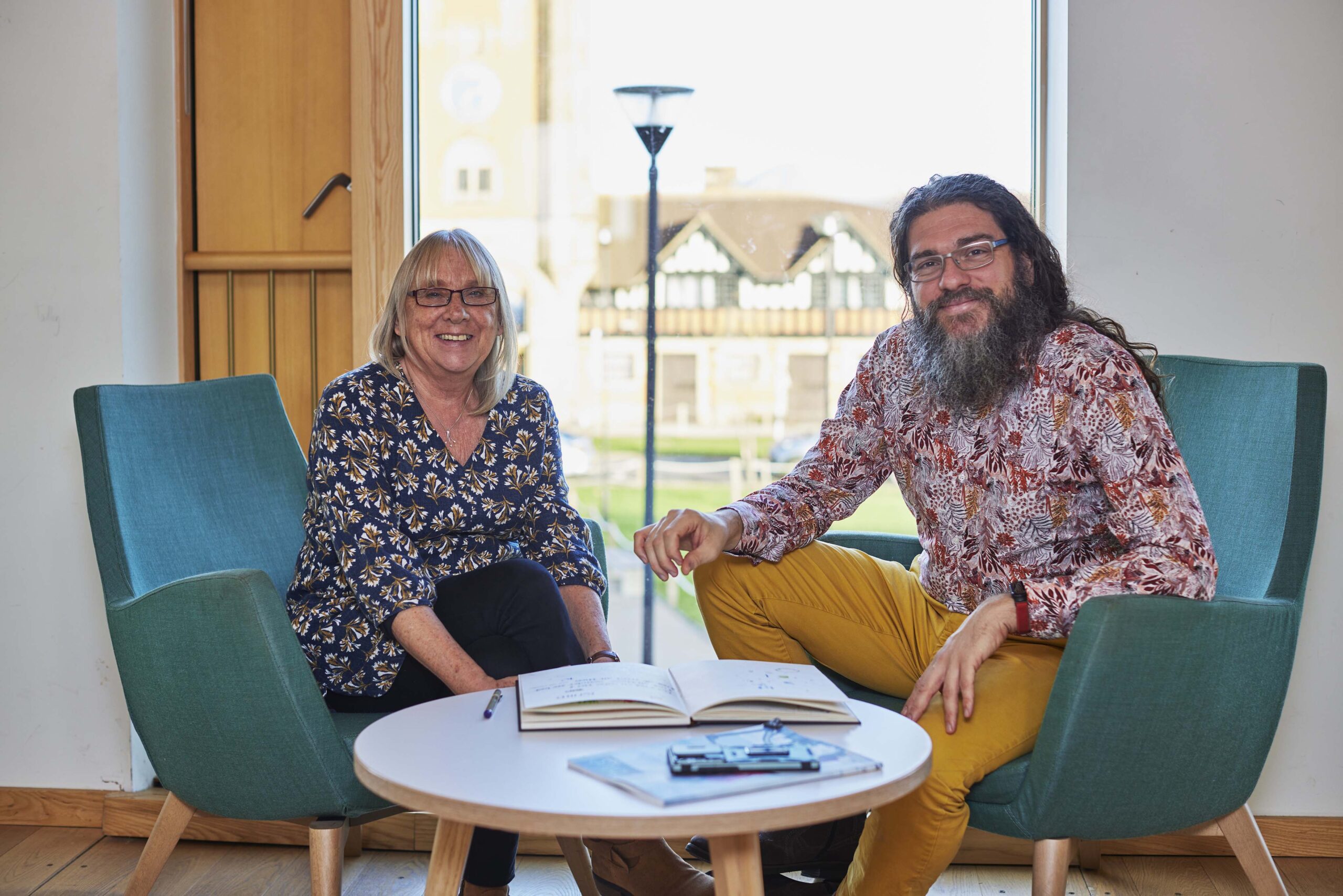 Giovanni Felice Pace and Gill Dawson, co-founders of The Metis Institute, seated outdoors at Worth School, the venue for our psychotherapy training, welcoming enquiries.
